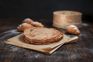 freshly baked sweet pancakes stacked on brown baking paper and croissants on a dark brown wooden table on a dark gray background
