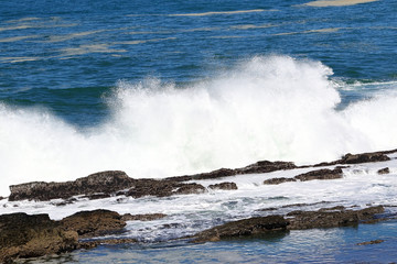 A big wave crashing into the rocks in the rough wild water of the ocean on a stormy during wintertime in South Africa.