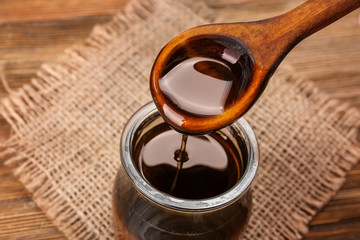 Spoon with tasty caramel sauce over jar, closeup