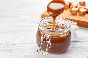 Spoon with tasty caramel sauce over jar on table
