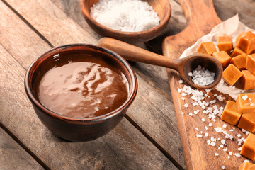 Bowl with tasty caramel sauce and candies on table
