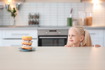 Plate with sweet donuts on table and little cute girl in kitchen