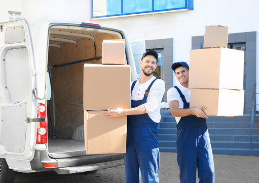 Delivery men with moving boxes near car