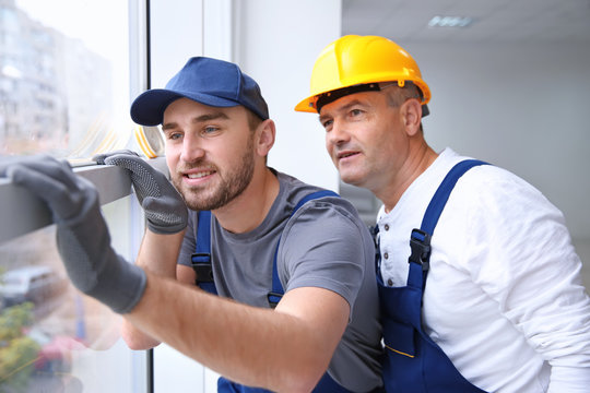 Construction Worker With Trainee Installing Window In House