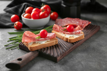 Delicious sandwiches with salami and cherry tomatoes on wooden board