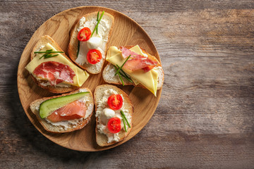 Plate with delicious sandwiches on wooden background, top view