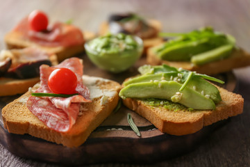 Wooden board with delicious sandwiches on table, closeup