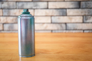 Aluminum aerosol can with paint on wooden table against brick wall