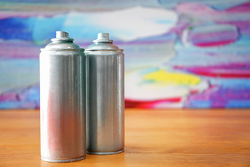 Aluminum aerosol cans with paints on wooden table against blurred background