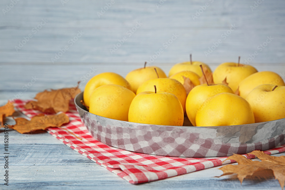 Poster metal dish with ripe yellow apples on table