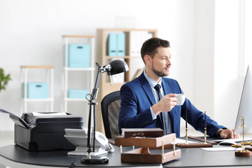 Young male notary drinking coffee in office