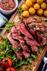 Juicy rare sliced grilled fillet steak served with tomatoes and roast vegetables on an old wooden board.