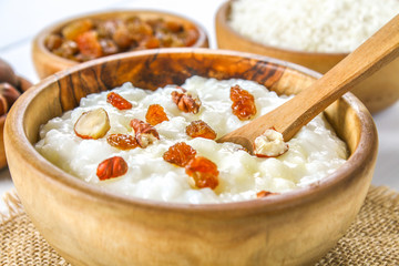 Rice milk porridge with nuts and raisins in wooden bowls on a white wooden table.
