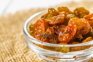 Golden Raisins from dried grapes in a glass bowl on sacking on a white wooden table of boards. Ingredients for cooking.