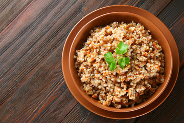 Boiled buckwheat in a bowl with pieces of chicken meat and cilantro on a brown wooden table.