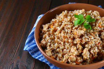 Boiled buckwheat in a bowl with pieces of chicken meat and cilantro on a brown wooden table.