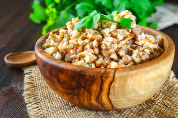 Boiled buckwheat in a bowl with pieces of chicken meat and cilantro on a brown wooden table.