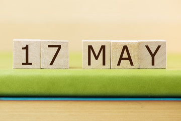 Wooden cube shape calendar for MAY 17 on green book, table.