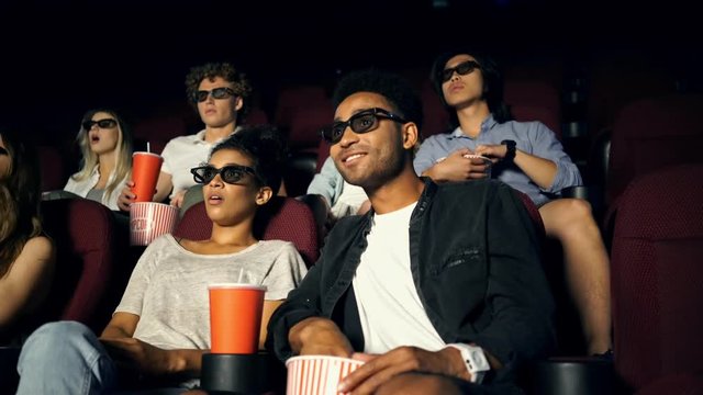 Shocked cheerful multiethnic young couples watching film with popcorn in cinema 