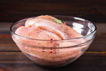 Raw chicken fillet in a glass bowl on the background of a wooden table. Meat ingredients for cooking.