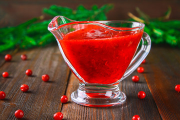 Cowberry cranberry sauce in a glass clear saucer on a wooden table with spruce branches.