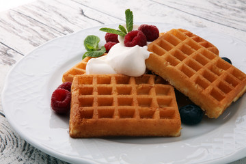 Plate of belgian waffles with whipped cream, mint and fresh berries