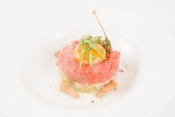 Smoked steak tartare served with egg yolk,  onion, pickle,  caper, mushroom and rocket salad on a white background