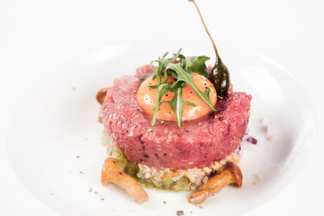 Steak tartare served with egg yolk,  onions, caper, mushroom and rocket salad on a white background