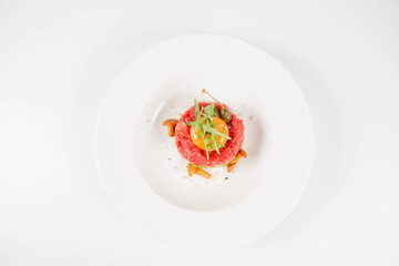 Steak tartare served with egg yolk,  onions, caper, mushroom and rocket salad on a white background
