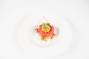 Steak tartare served with egg yolk,  onions, caper, mushroom and rocket salad on a white background