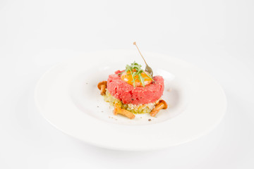 Steak tartare served with egg yolk,  onions, caper, mushroom and rocket salad on a white background
