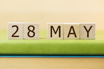 Wooden cube shape calendar for MAY 28 on green book, table. 