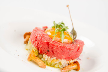 Steak tartare served with egg yolk,  onion, pickle,  caper, mushroom and rocket salad on a white background