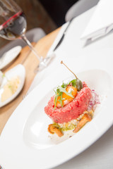 Steak tartare served in a restaurant with egg yolk,  onion, pickles, caper, mushroom and rocket salad