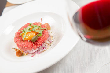 Steak tartare served in a restaurant with egg yolk,  onion, pickles, caper, mushroom and rocket salad