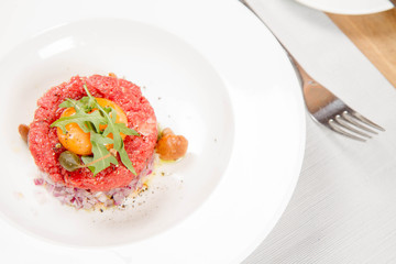 Steak tartare served in a restaurant with egg yolk,  onion, pickles, caper, mushroom and rocket salad