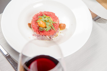 Steak tartare served in a restaurant with egg yolk,  onions, caper, mushroom and rocket salad