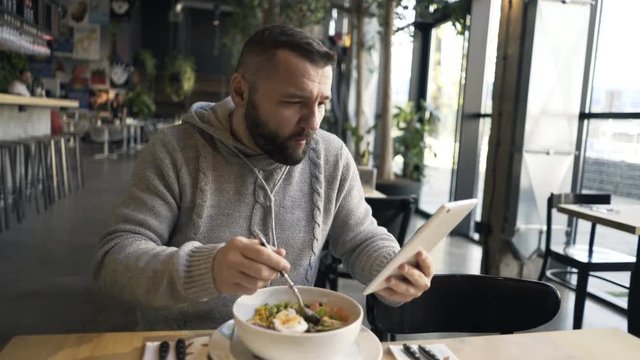 Man with tablet eating salad in cafe
