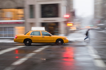 Fototapeta na wymiar Panning motion image of a New York City yellow taxi cab in the snow as it passes through an intersection and past a pedestrian