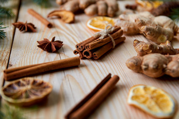 Fototapeta na wymiar Cinnamon sticks with anise stars, ginger, dried oranges on the wooden background decorated with Christmas tree branches. Traditional spices for mulled wine, Christmas bakery. New Year composition