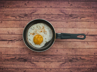 Pan with fried egg on a wooden background with text space.
