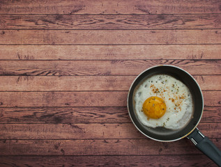 Closeup view of the fried egg on a pan on the wooden table.