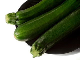 Three zucchinis on black plate, isolated on white background