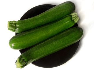 Three zucchinis on black plate, isolated on white background