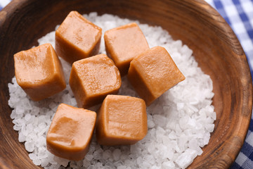 Wooden bowl with salt and caramel candies, closeup