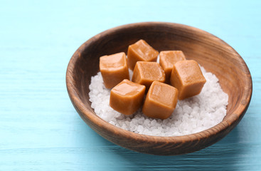 Bowl with salt and caramel candies on color wooden background