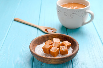 Bowl with salt and caramel candies on color wooden background