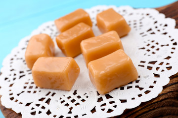 Wooden board with tasty caramel candies on table, closeup