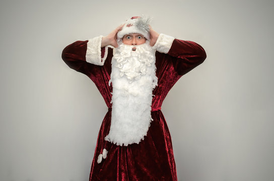 Surprised Santa Claus in stress holds a hands on a head isolated on a gray background.