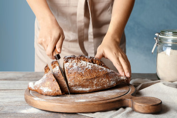 Woman cutting buckwheat bread on wooden board in kitchen